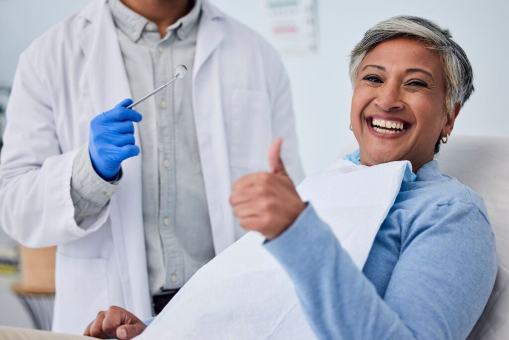 A smiling woman giving a thumbs-up at her dental appointment