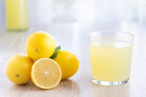 Pile of lemons next to glass of lemon juice